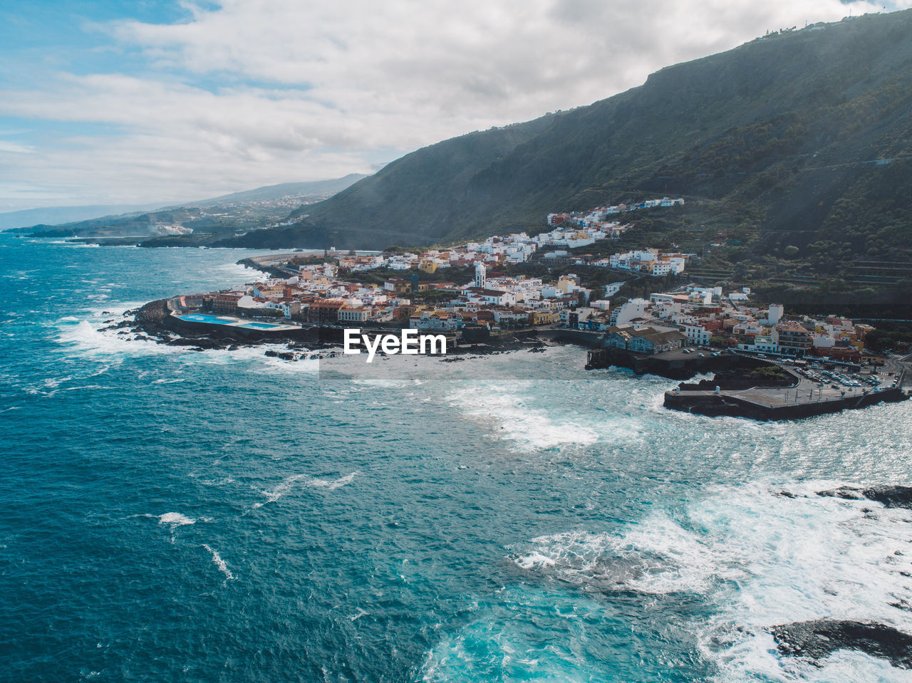 Aerial view of sea by mountains against sky