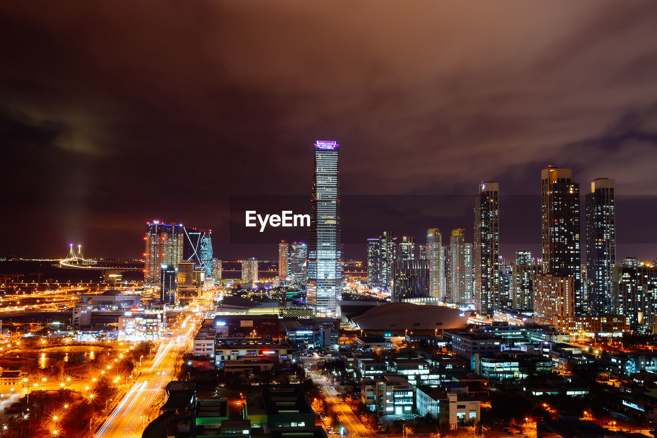 Illuminated cityscape against cloudy sky at night