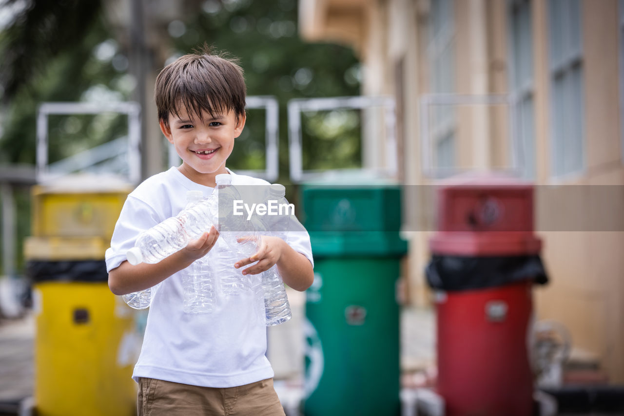 PORTRAIT OF HAPPY BOY STANDING AGAINST BLURRED BACKGROUND