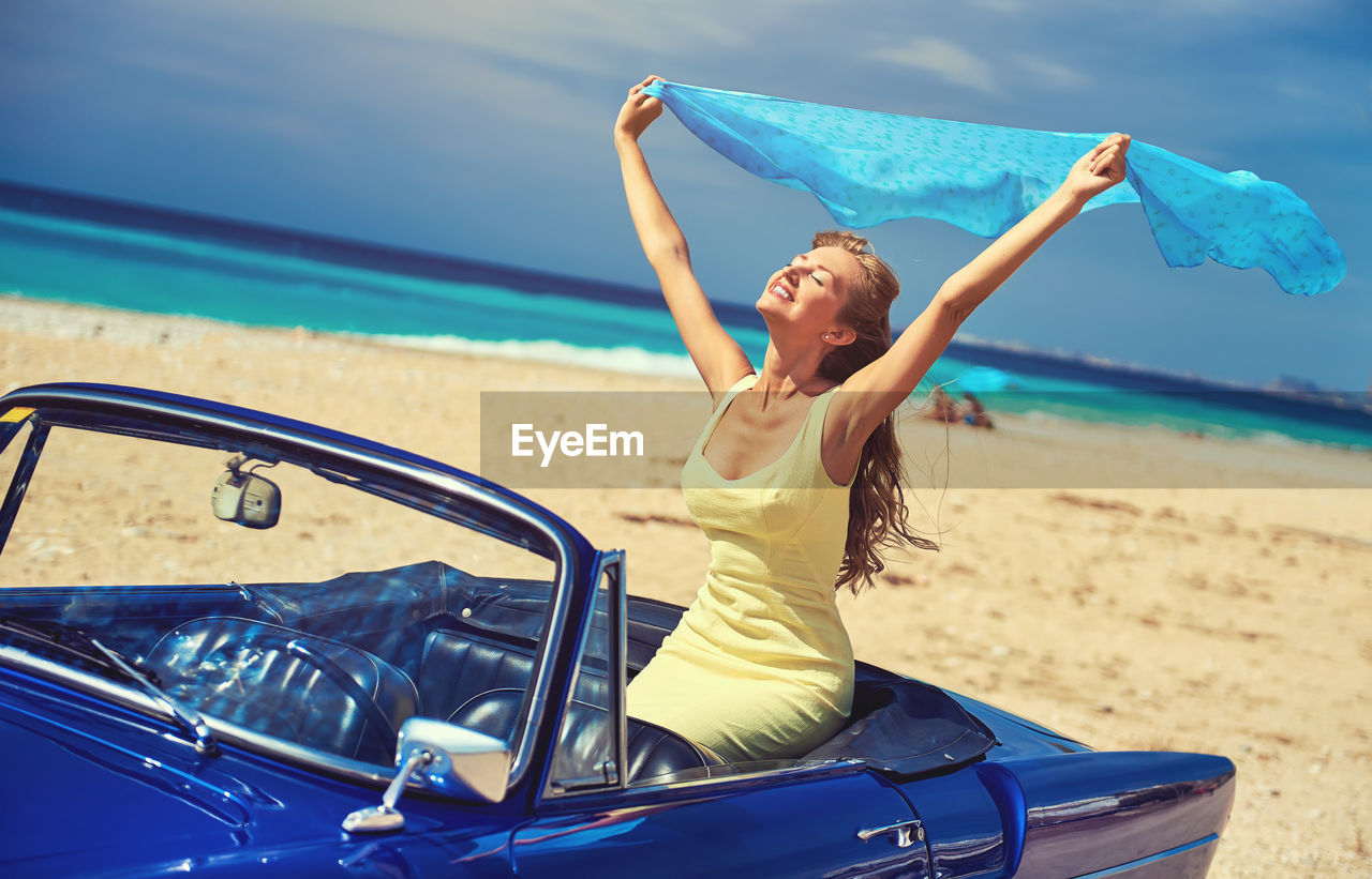 Portrait of smiling young woman in car on beach 