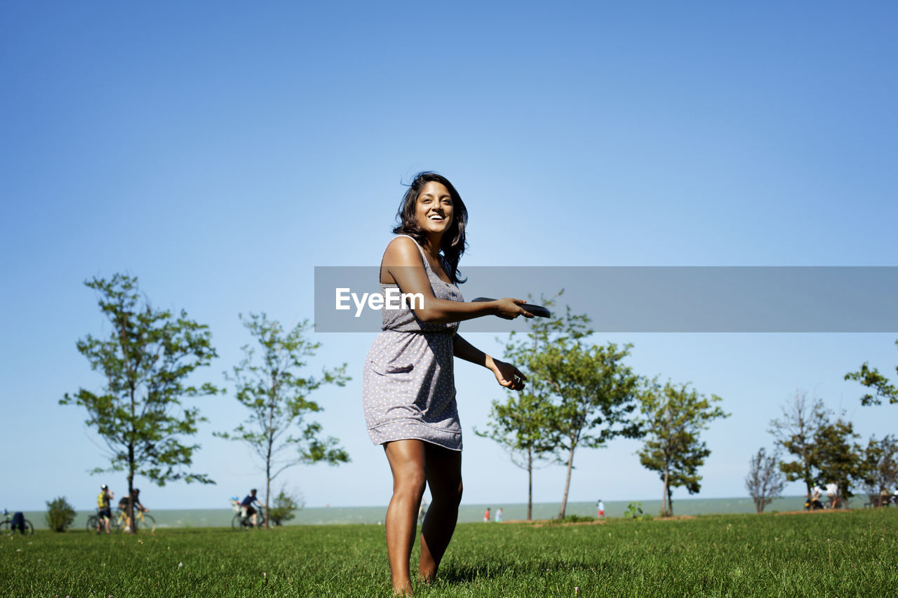 Playful woman throwing plastic disc while standing at park