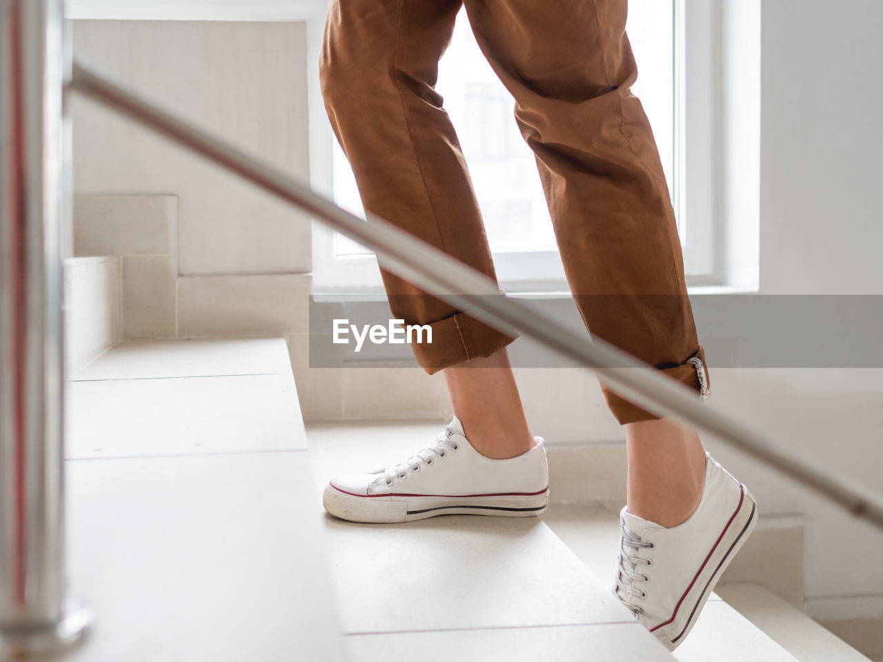 Woman in white sneakers and khaki trousers goes upstairs to her apartment. white staircase. 