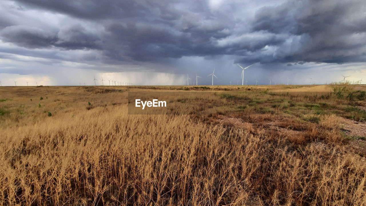 Scenic view of field with wind turbines against cloudy sky