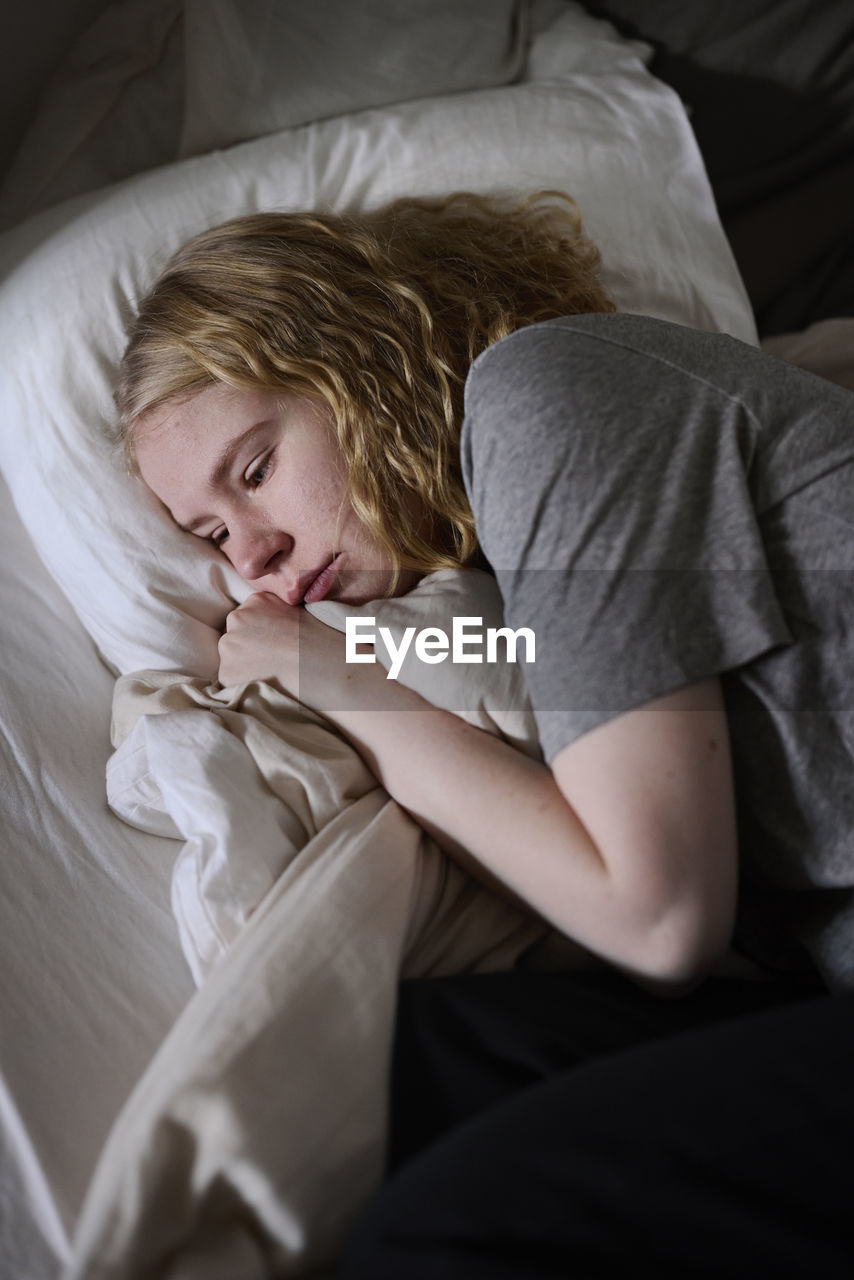 Crying young woman lying in bed