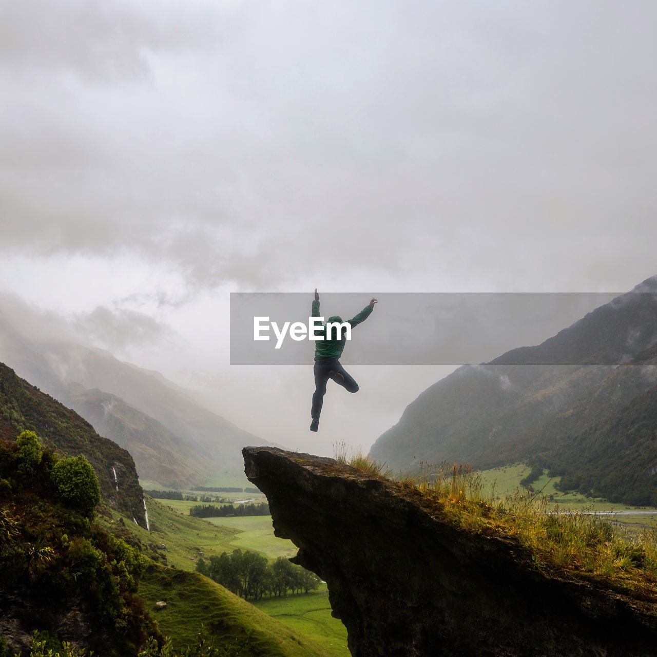 Man jumping over mountain against cloudy sky during foggy weather