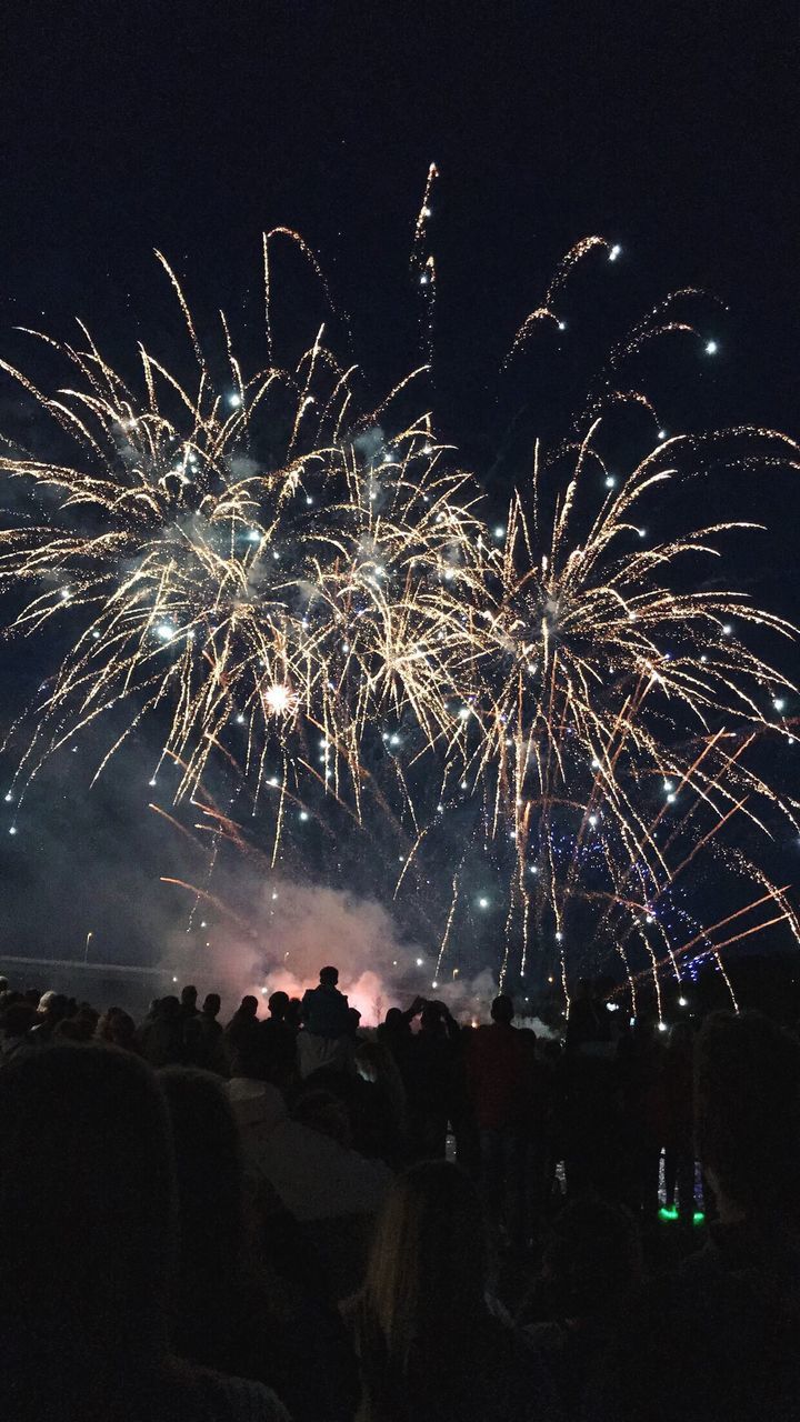 Low angle view of crowd watching firework display at night