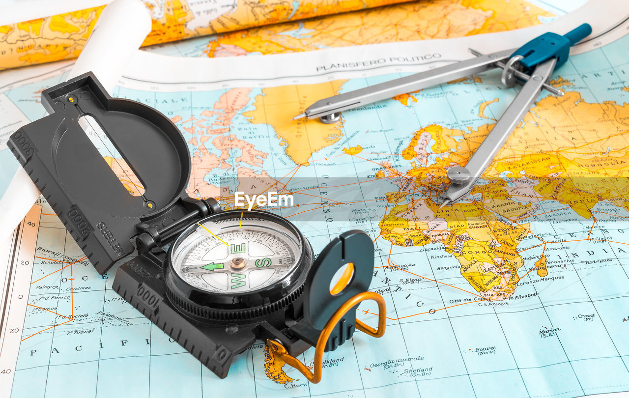 High angle view of navigational compass and drawing compass on world map