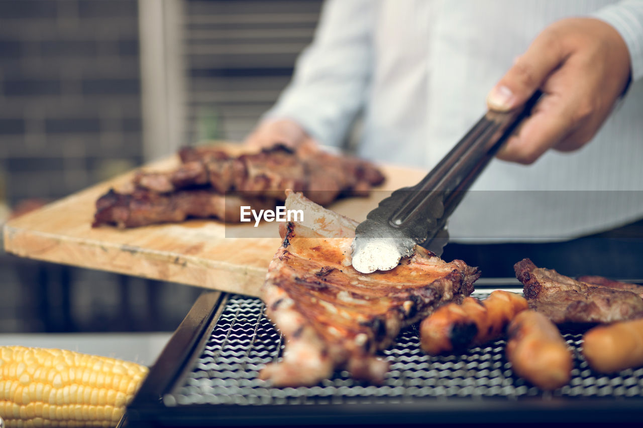 Midsection of man preparing meat on barbecue grill