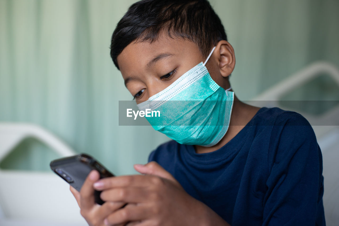 Boy wearing mask using mobile phone at hospital