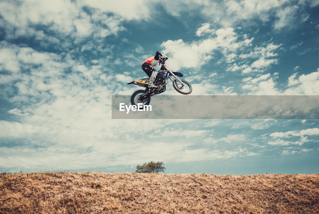Low angle view of man jumping while riding motorcycle against sky