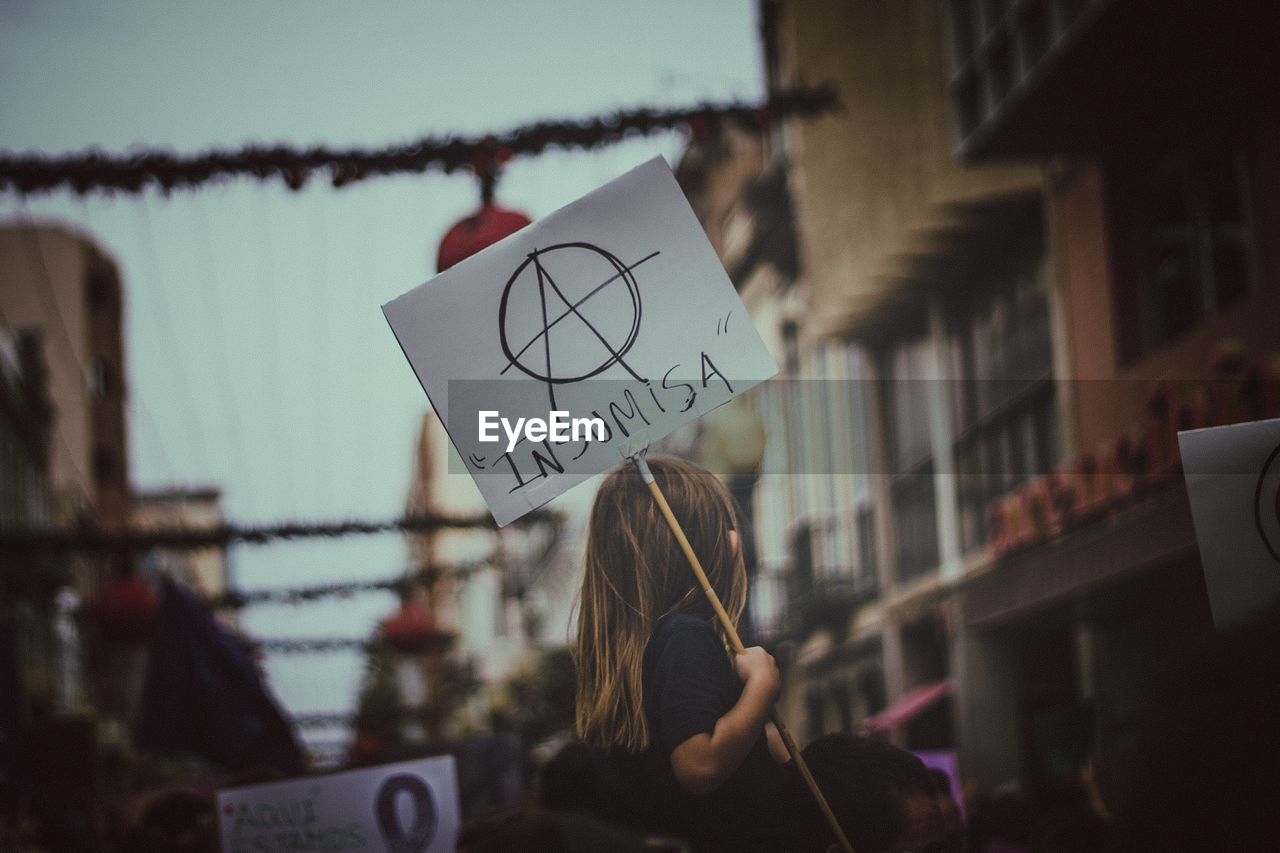 Low angle view of girl holding placard in city