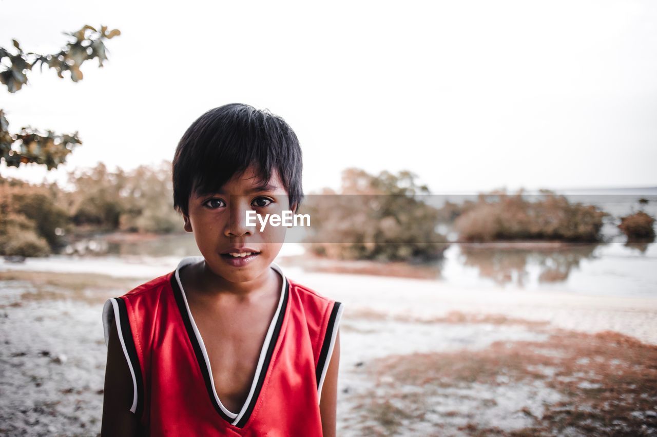 Portrait of boy standing at beach against sky