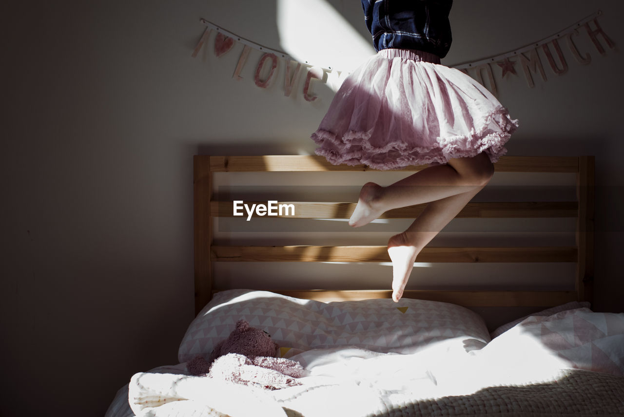 Low section of playful girl wearing skirt while jumping on bed at home