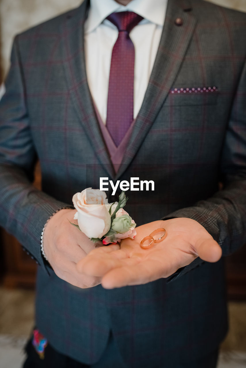 Midsection of groom holding flowers and rings during wedding ceremony
