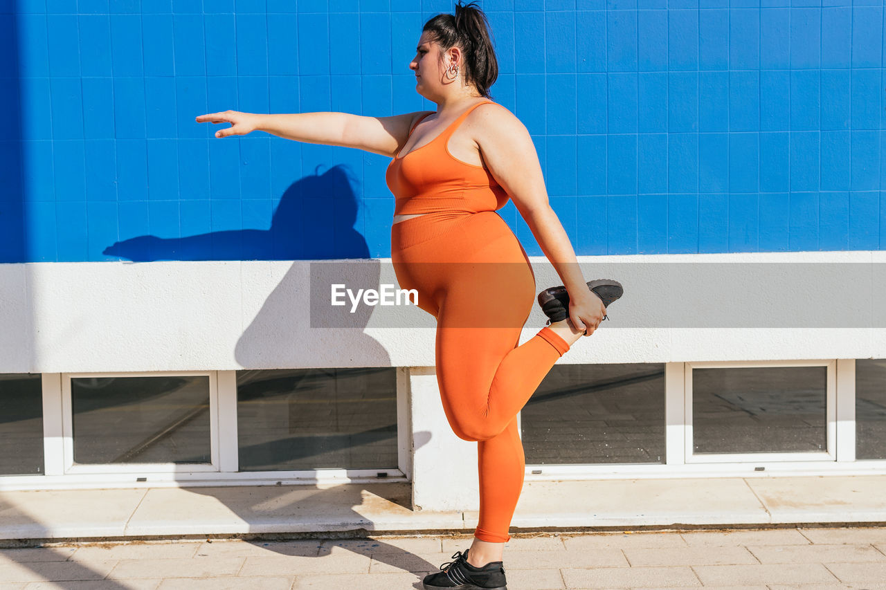 Side view of plump female athlete in sportswear exercising on tiled walkway in sunny town