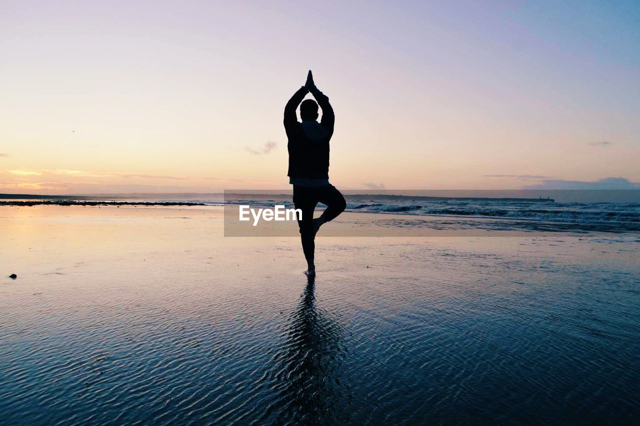 Man doing the tree pose on beach