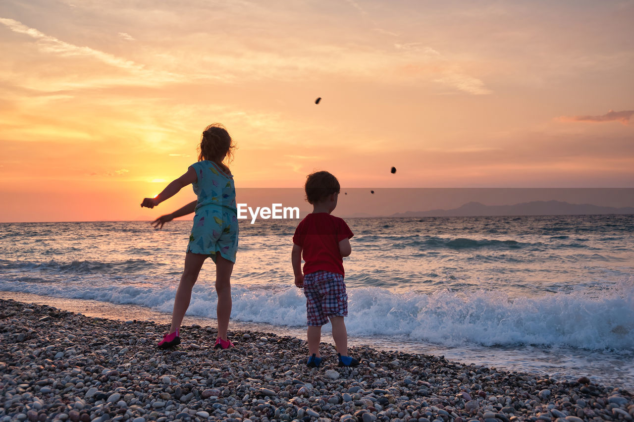 Summer memories. children throwing pebbles to sea during sunset.