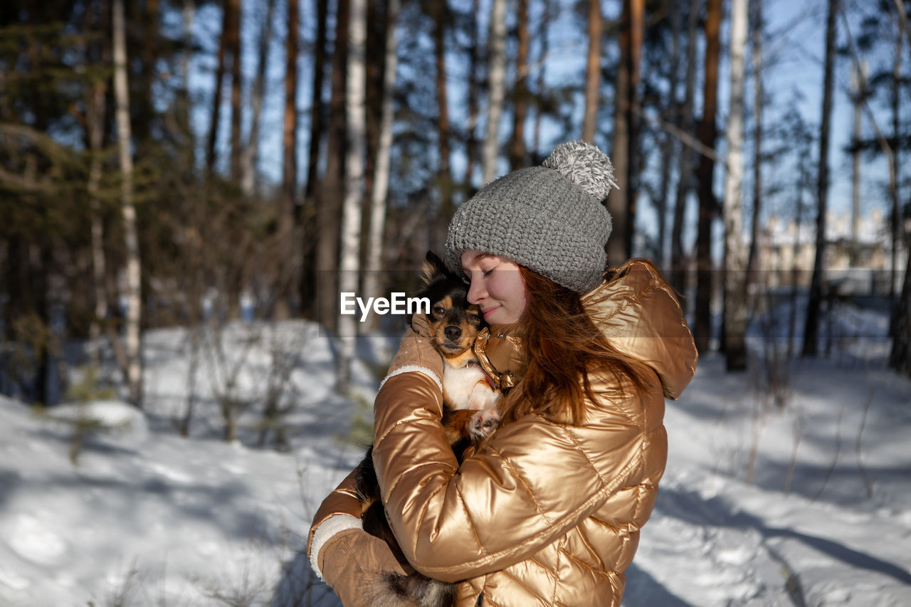 A young girl in the forest in winter holds a dog in her arms and enjoys the weather 