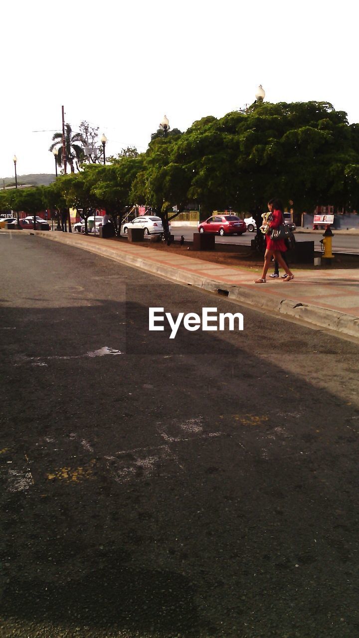 People walking on sidewalk by road against clear sky