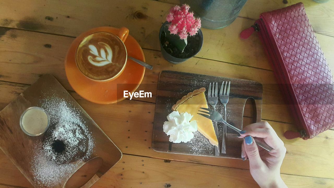 Cropped hand of woman eating cake on wooden table