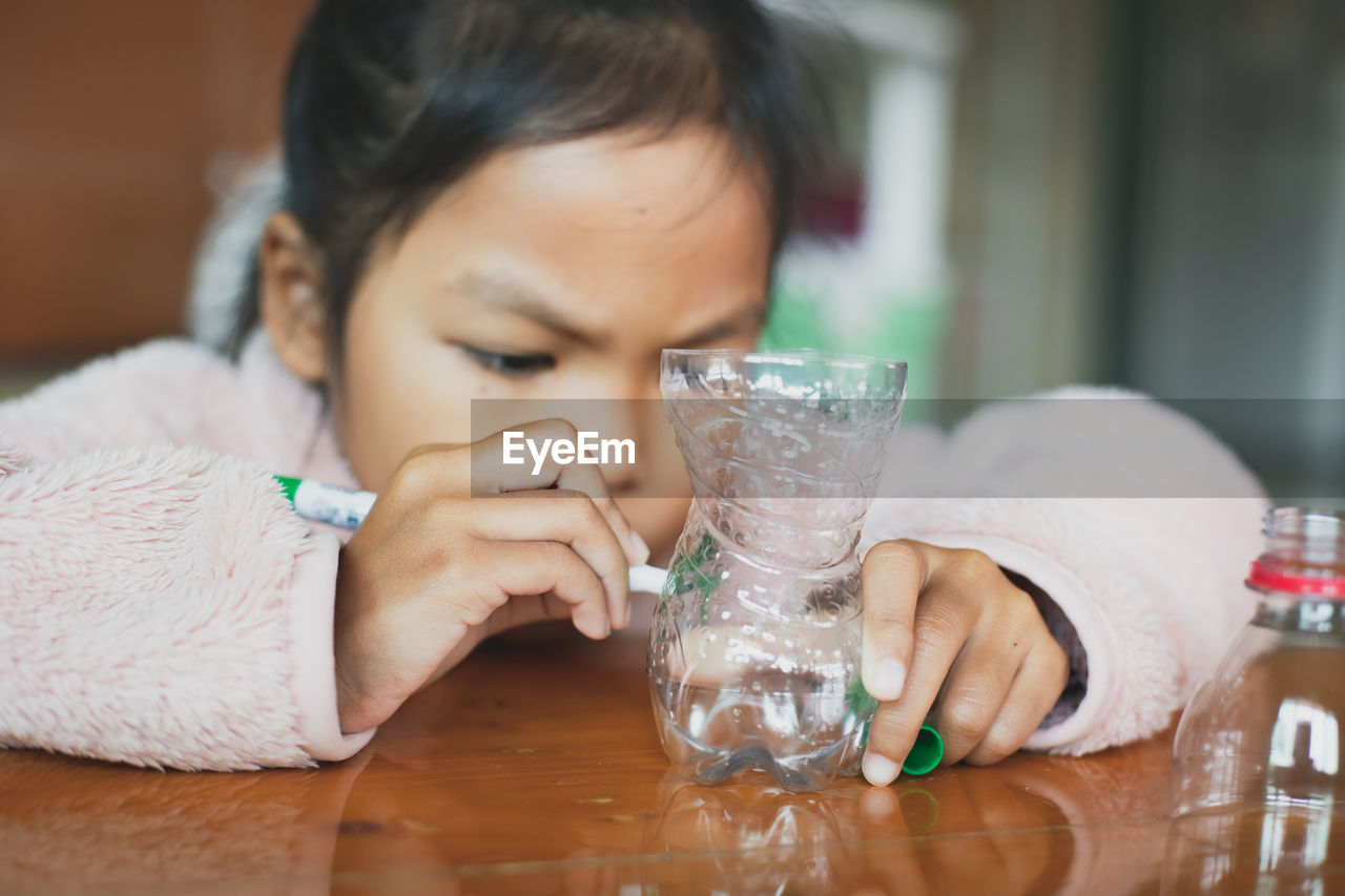 Girl decorating plastic bottle on table at home