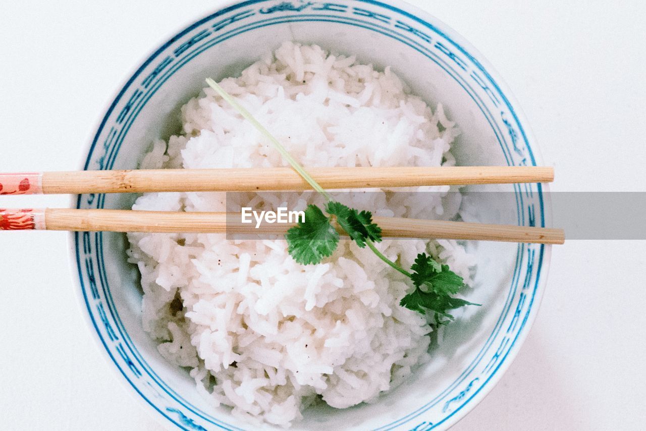 Directly above shot of rice in bowl with chopsticks over white background