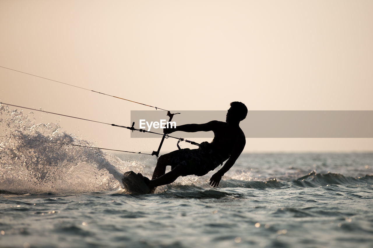 Silhouette man wakeboarding in sea against sky during sunset