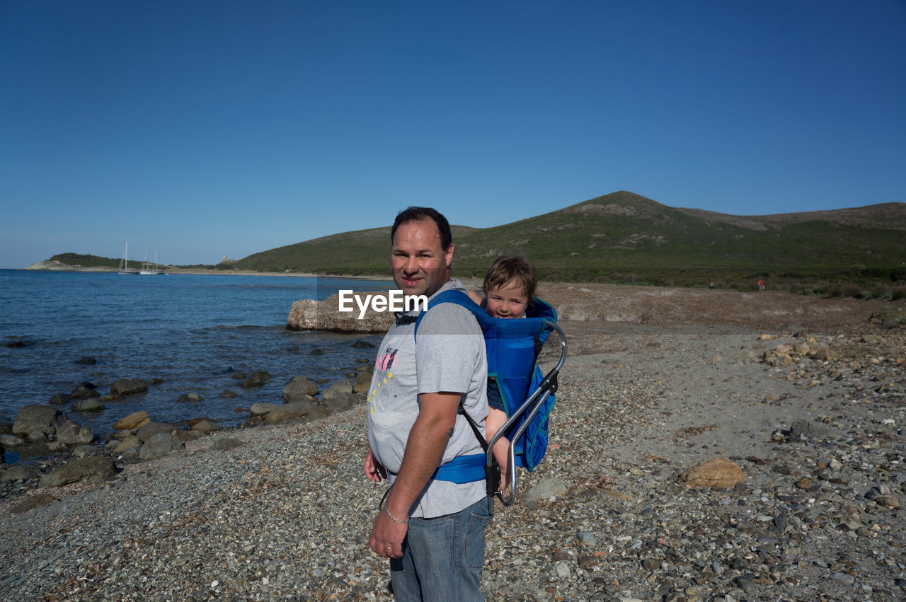 Portrait of man carrying boy in carriage at beach