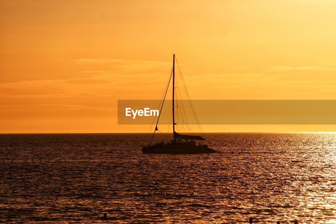 Sailboat sailing on sea against orange sky