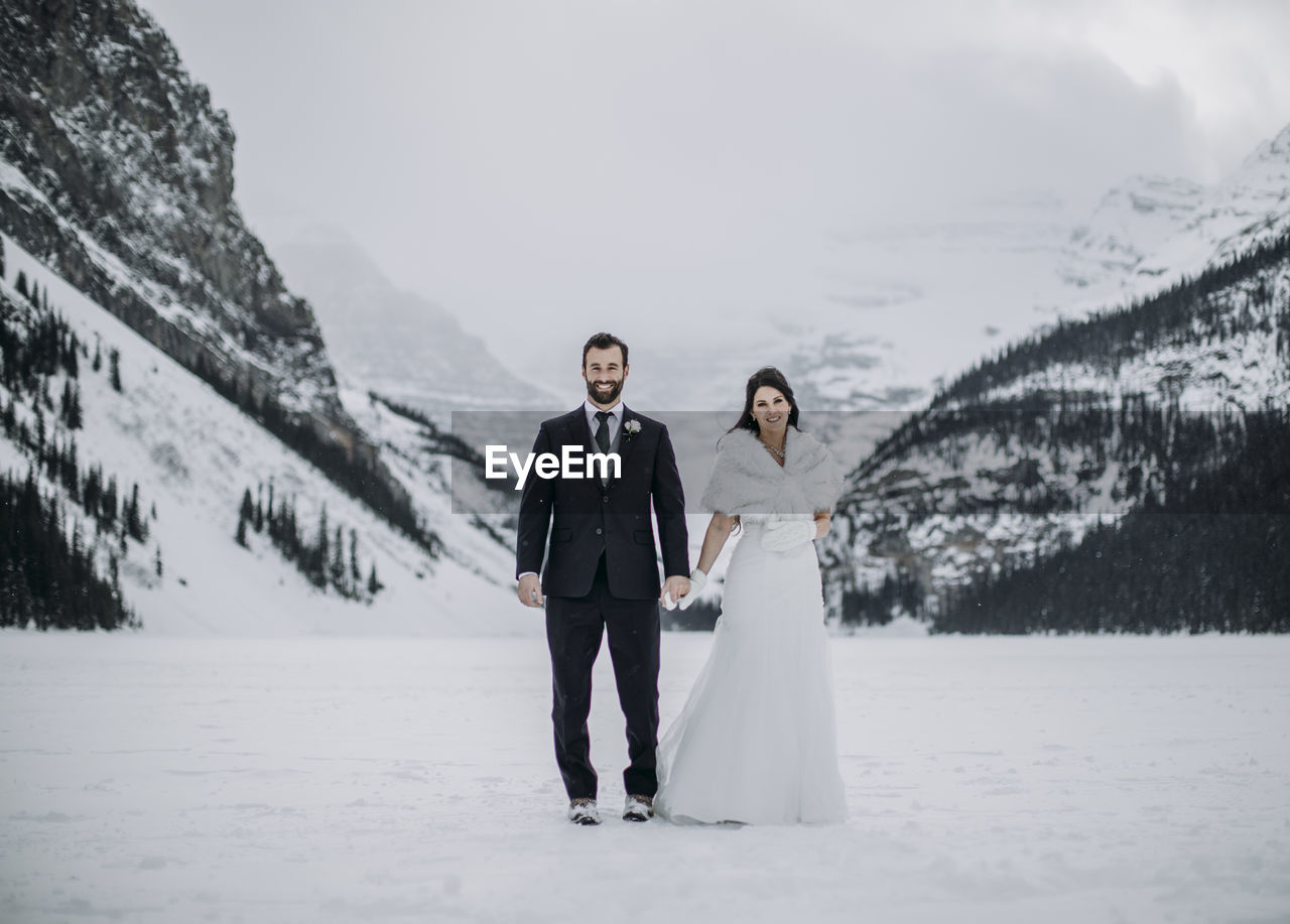 Newlywed couple stand on frozen lake louise, alberta canada in winter