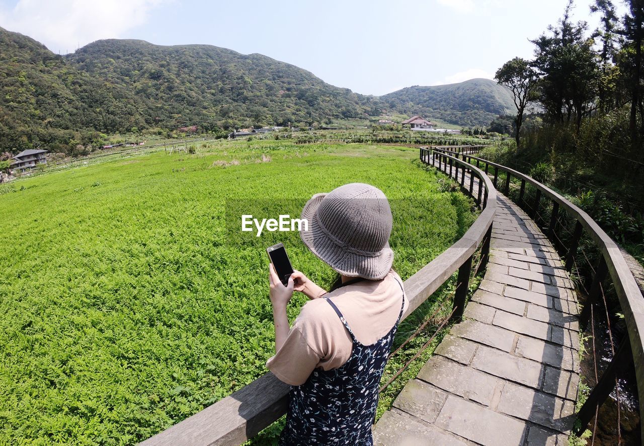 REAR VIEW OF WOMAN ON LANDSCAPE AGAINST MOUNTAIN