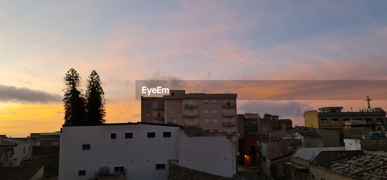 HIGH ANGLE VIEW OF BUILDINGS AND TREES AGAINST SKY AT SUNSET