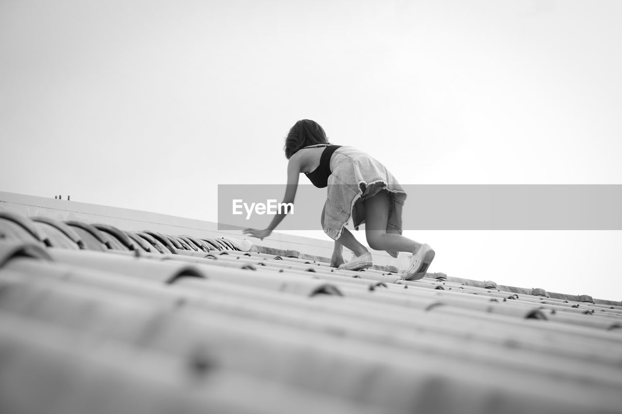 Low angle view of girl on roof against sky