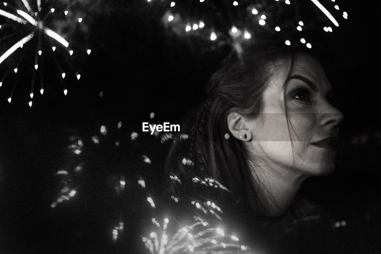 Double exposure image of thoughtful woman and firework display at night