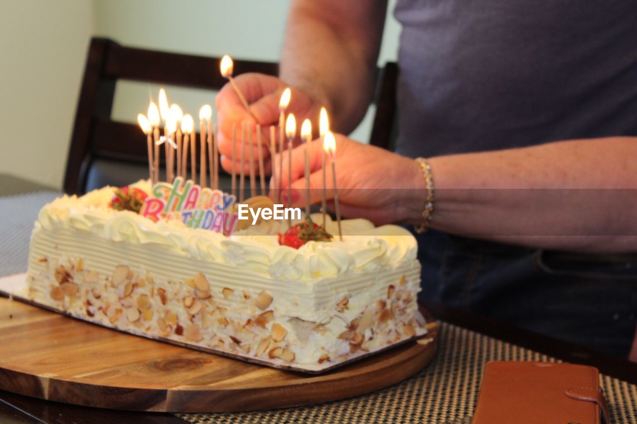 Cropped hands burning birthday candles on cake