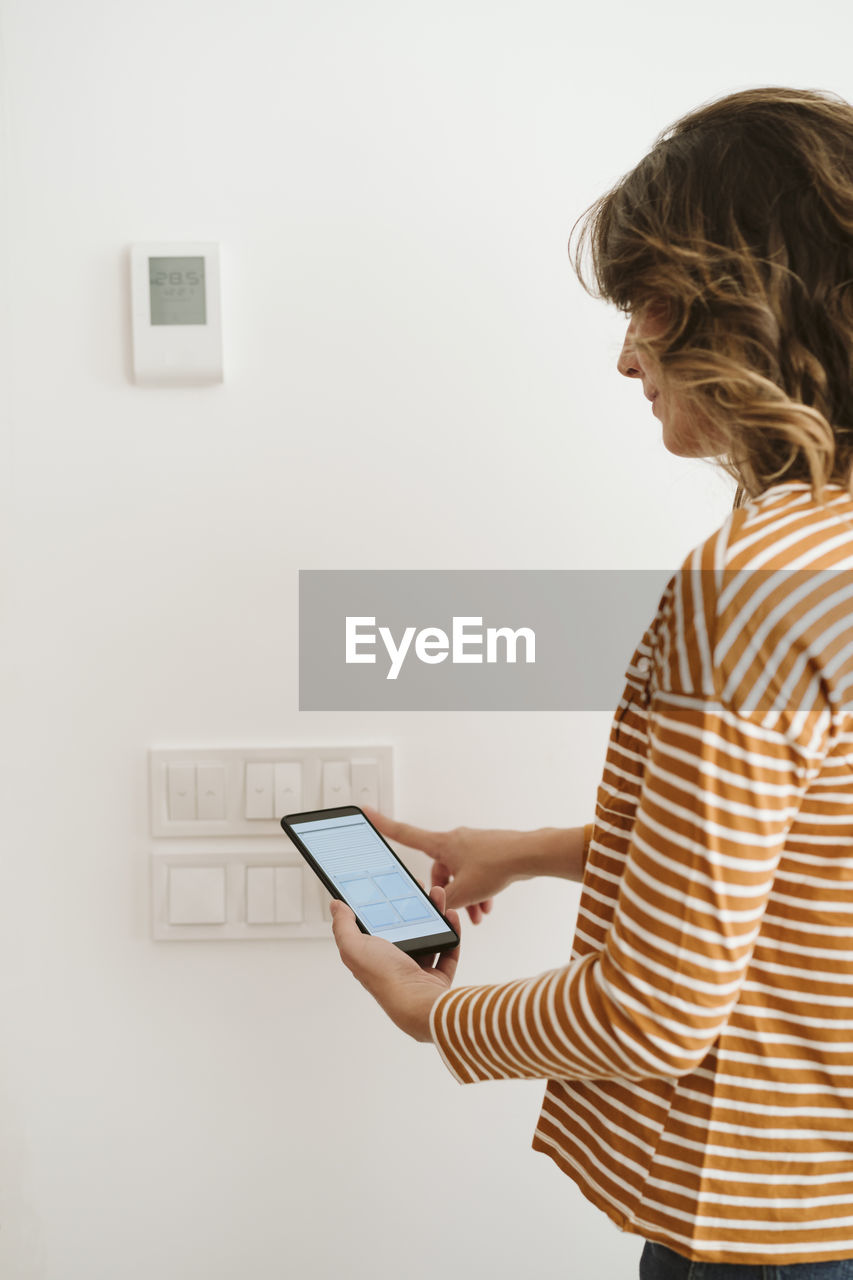 Young woman touching switch for blinds while checking mobile phone app