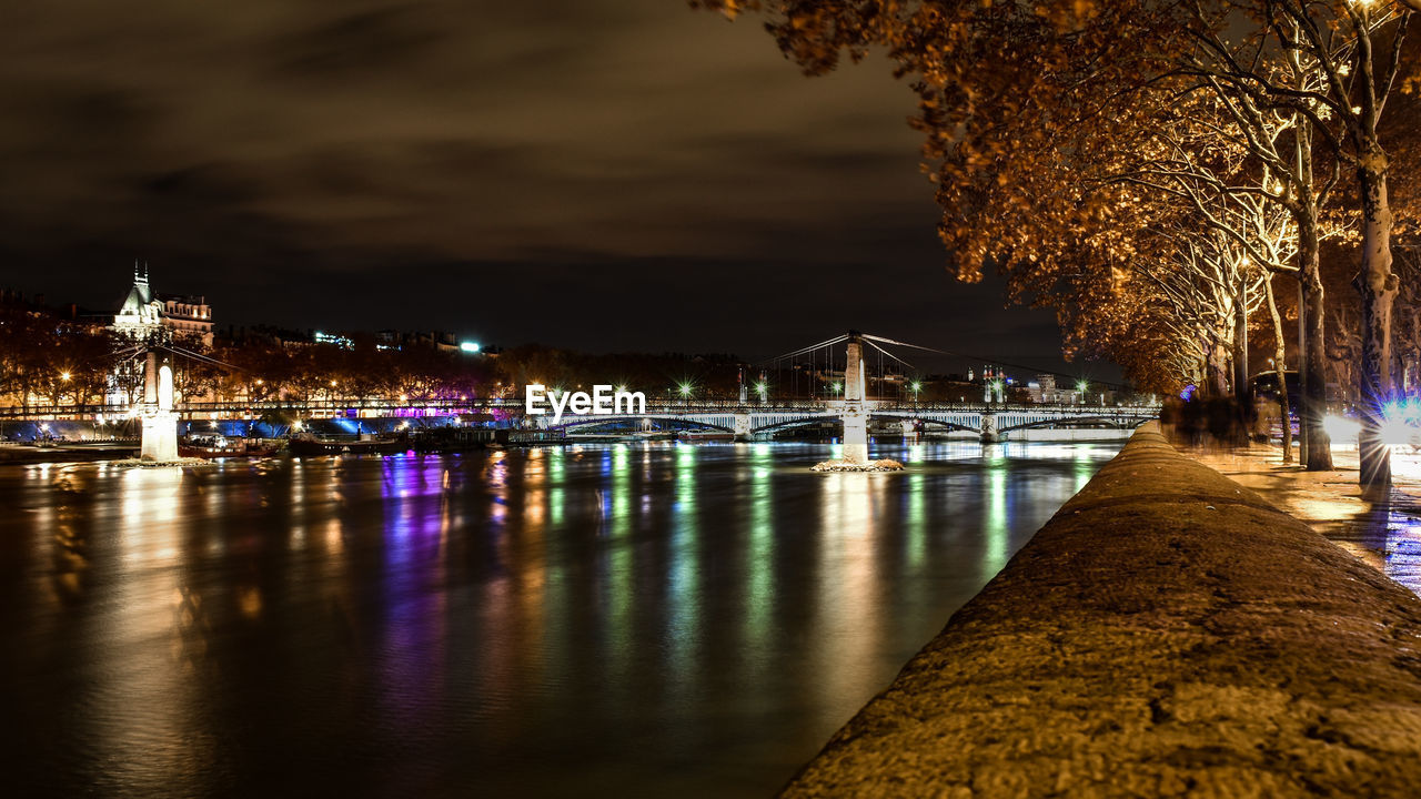 ILLUMINATED BRIDGE OVER RIVER AGAINST SKY AT NIGHT