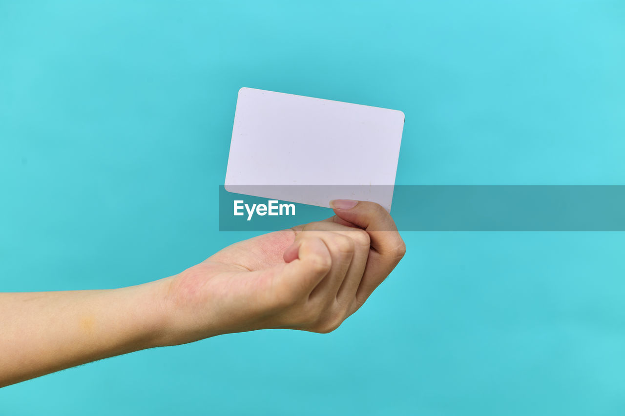 Female hand holding a blank business card on light blue studio isolated background