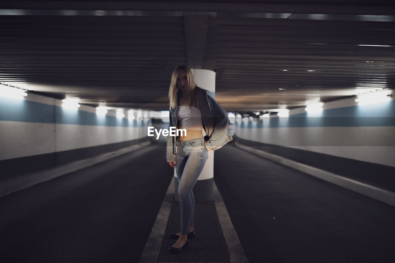 Portrait of serious woman standing under illuminated tunnel