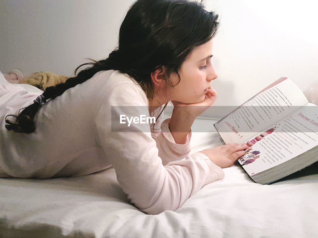 Girl reading book while lying on bed at home