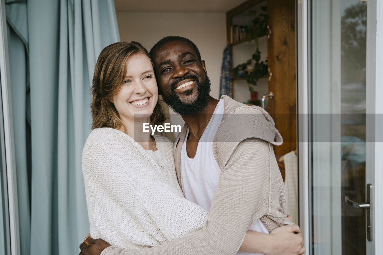 Happy multiracial couple embracing each other at doorway