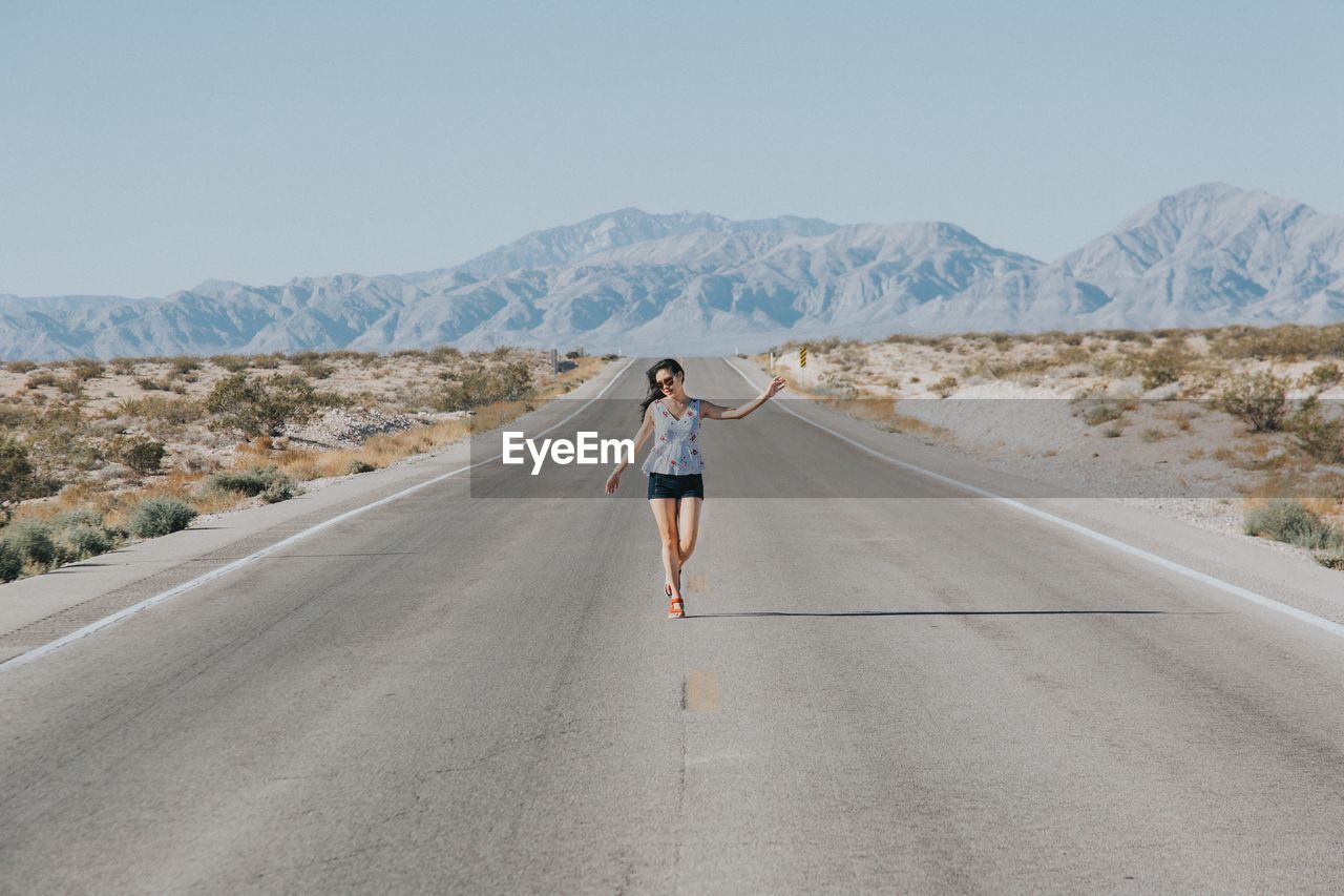 Full length of woman walking on country road against mountains and clear sky