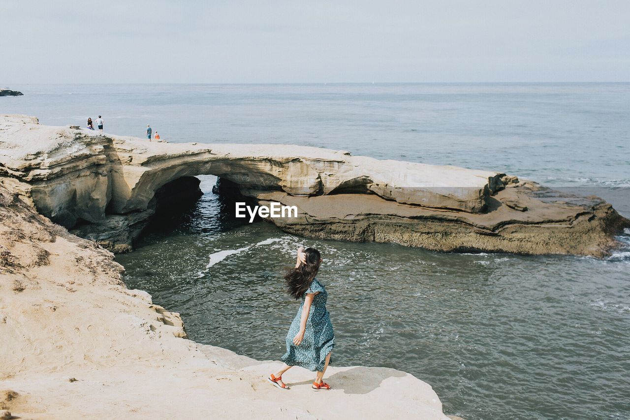 High angle view of woman standing on cliff at beach against sky