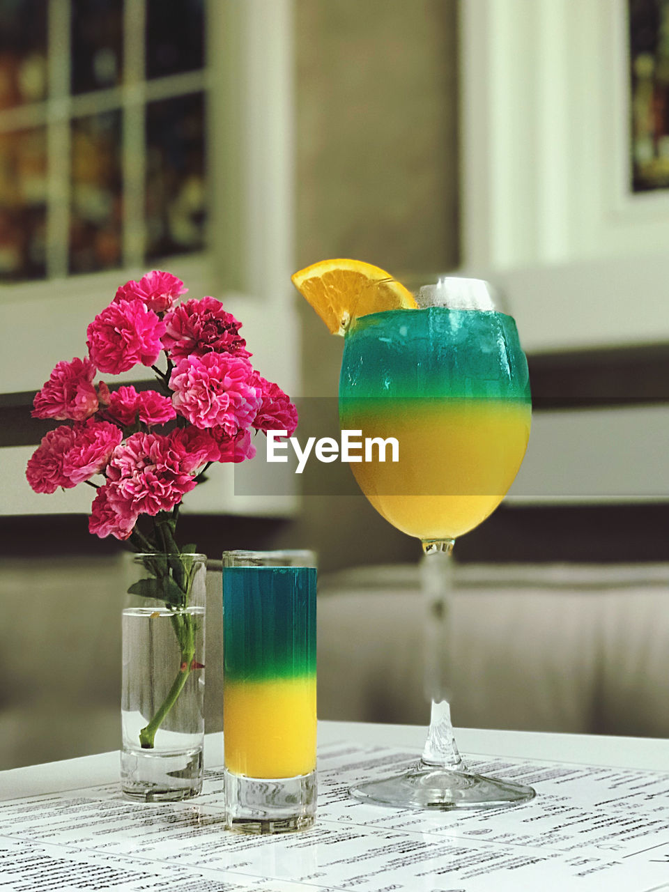 flower, flowering plant, glass, drink, refreshment, food and drink, freshness, drinking glass, cocktail, table, soft drink, yellow, plant, nature, alcohol, household equipment, fruit, no people, food, juice, vase, alcoholic beverage, still life, outdoors, beauty in nature, focus on foreground, summer, close-up, healthy eating, flower arrangement, citrus fruit