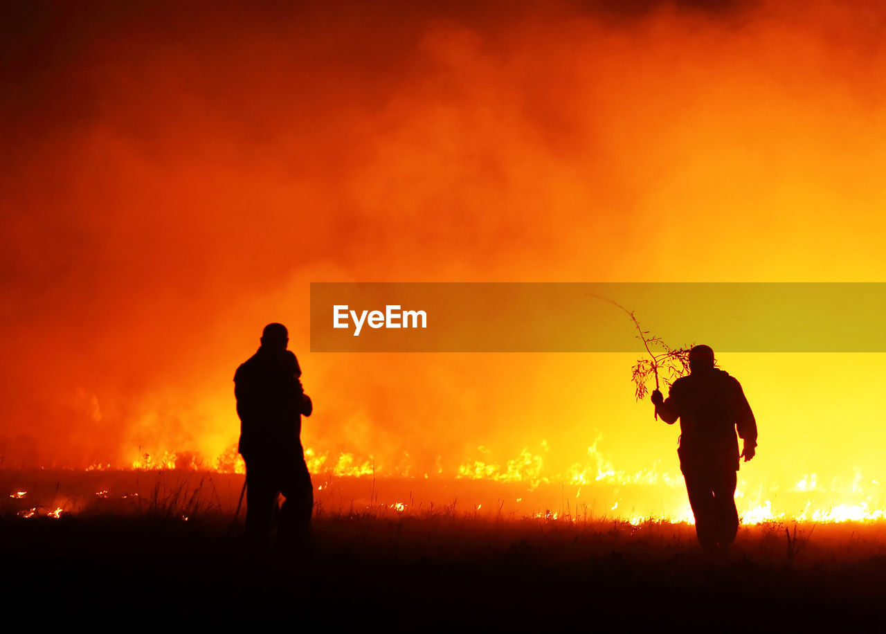 Silhouette firefighters working on burning gassy field