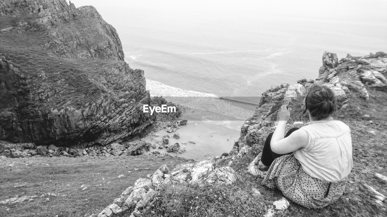 Woman looking at sea while sitting on cliff