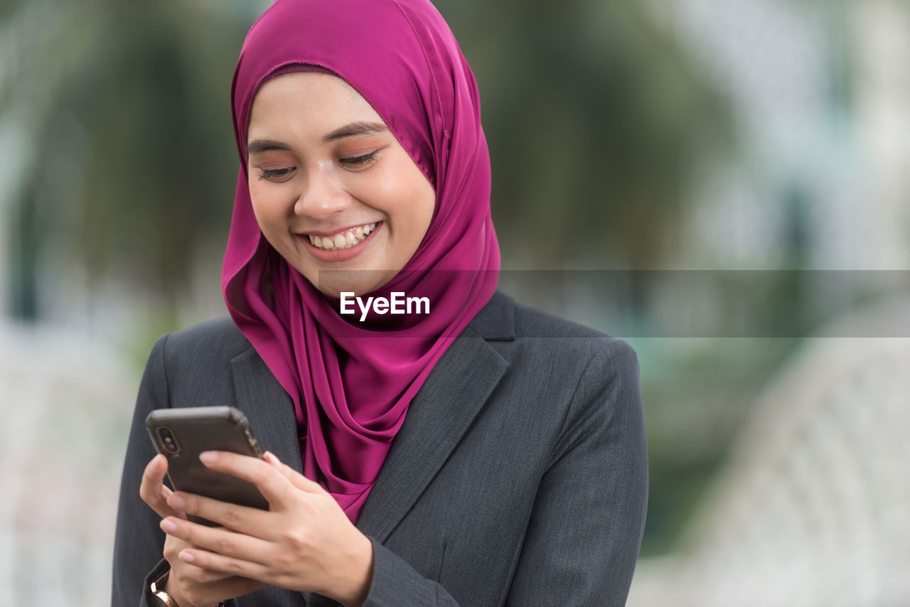 PORTRAIT OF A SMILING YOUNG WOMAN USING MOBILE PHONE