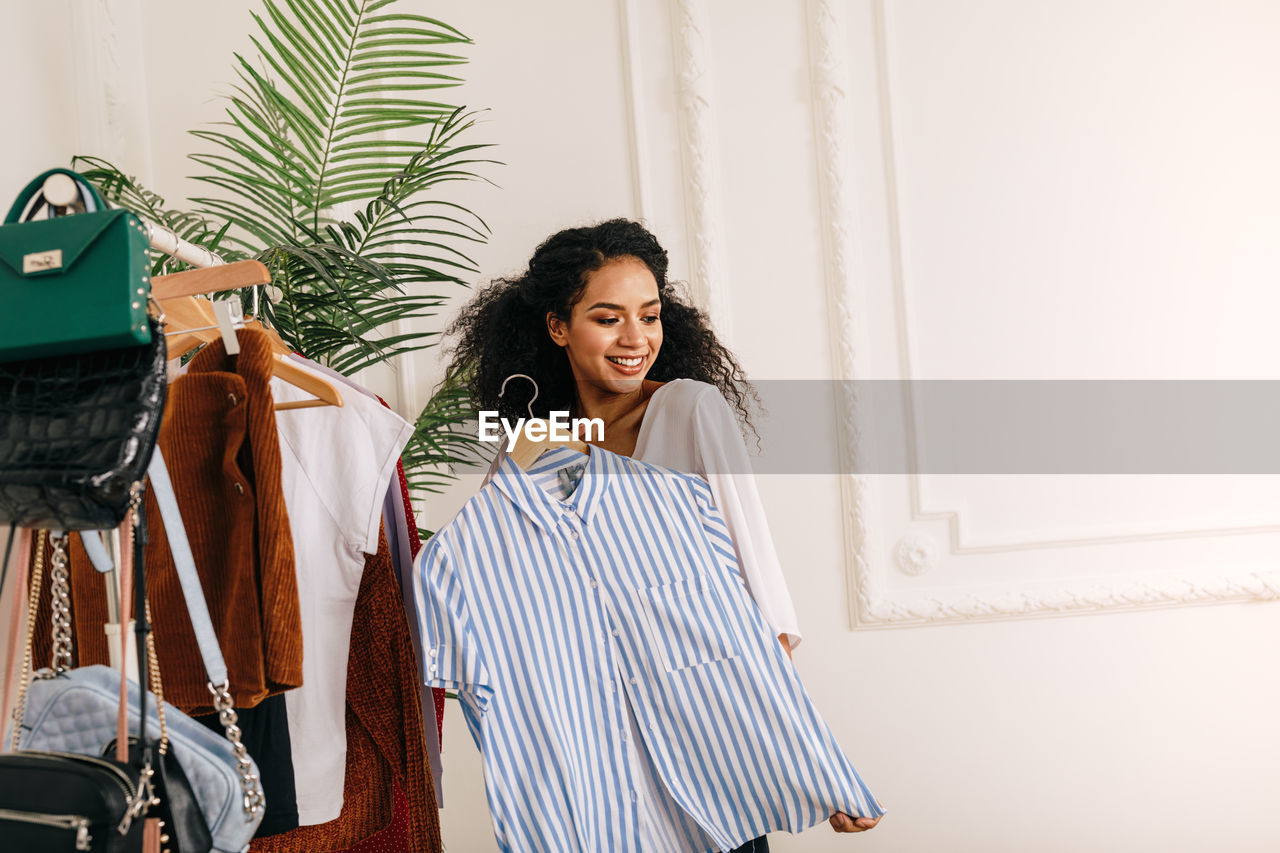 Smiling young woman holding top at home