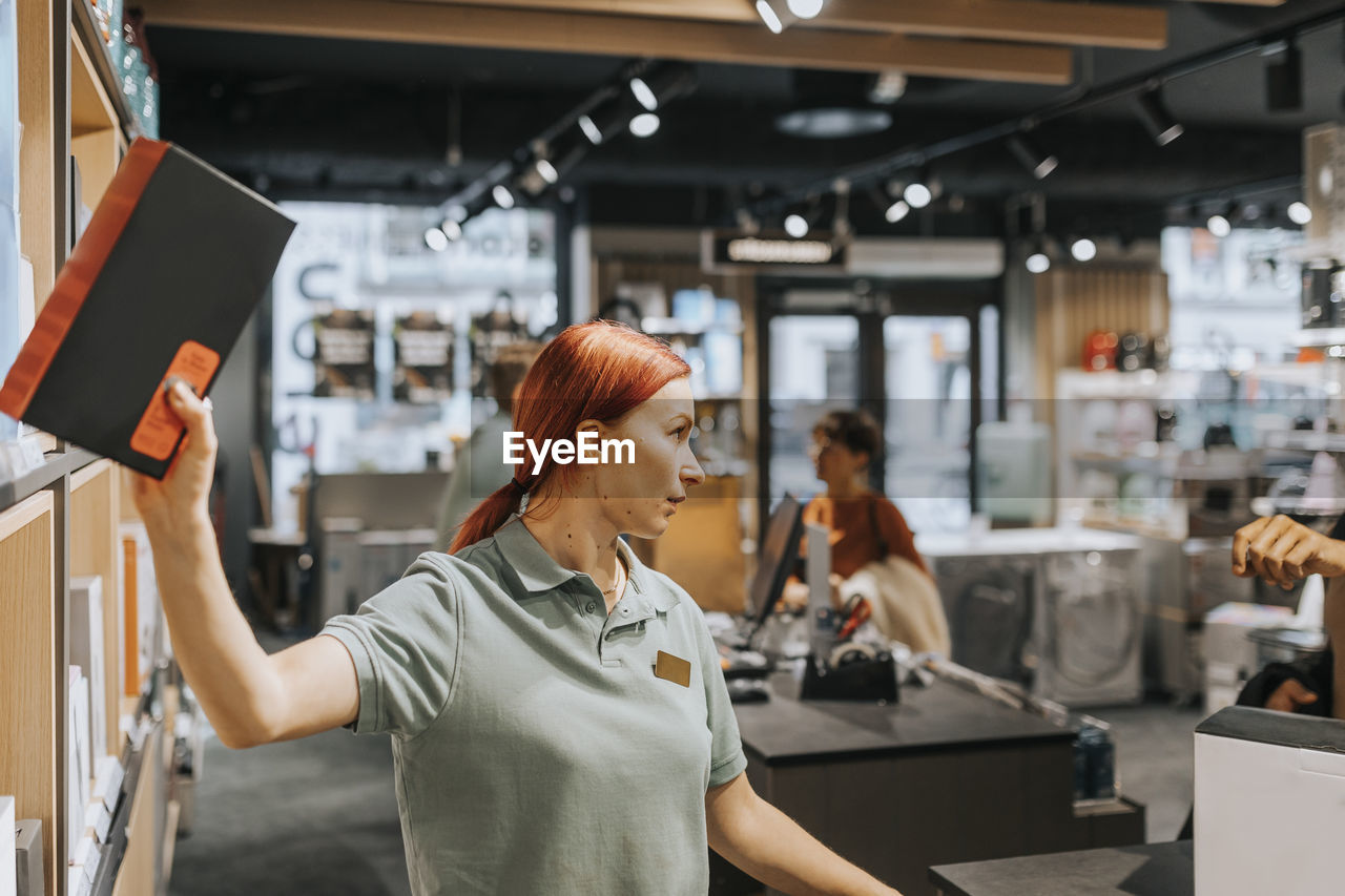 Redhead female sales clerk removing appliance from rack at electronics store