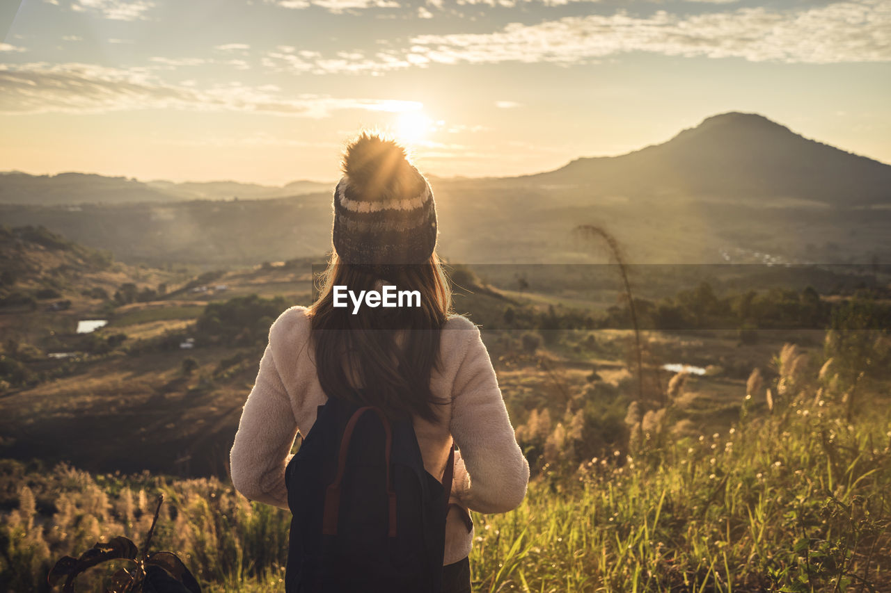 Rear view of woman standing on mountain against sky during sunset